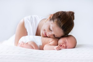 43360718 - young mother hugging her newborn child. mom nursing baby. woman and new born boy relax in a white bedroom. family at home. love, trust and tenderness concept. bedding and textile for nursery.